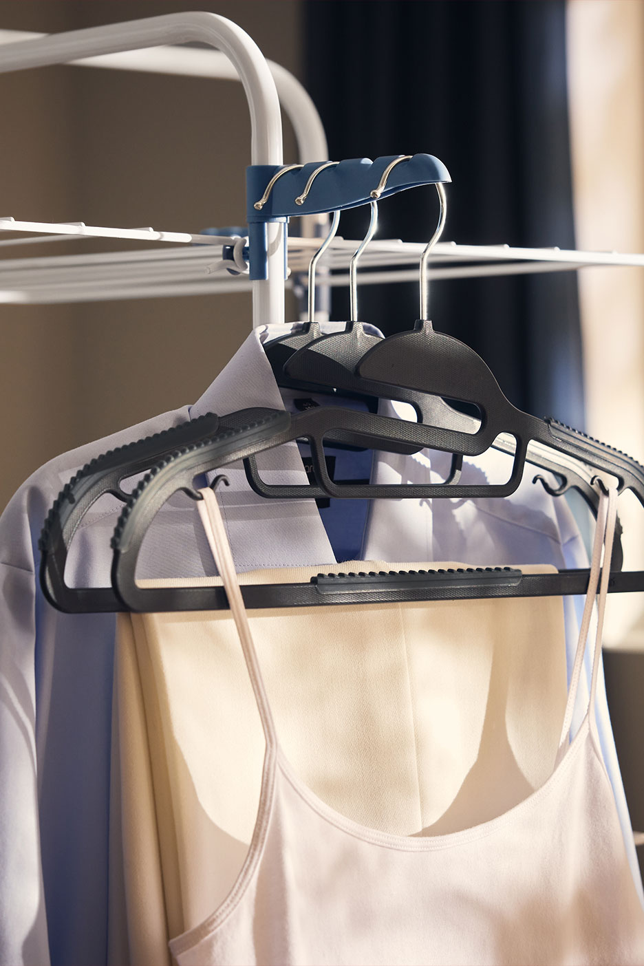 Cintres avec chemise, pantalon et débardeur, suspendus sur un étendoir.