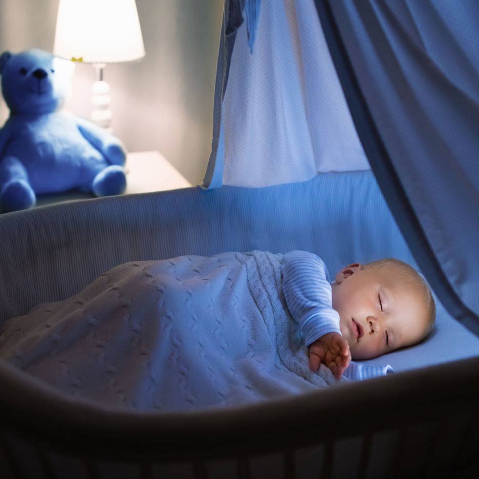 Bébé endormi dans un berceau avec un ours en peluche bleu et une veilleuse.