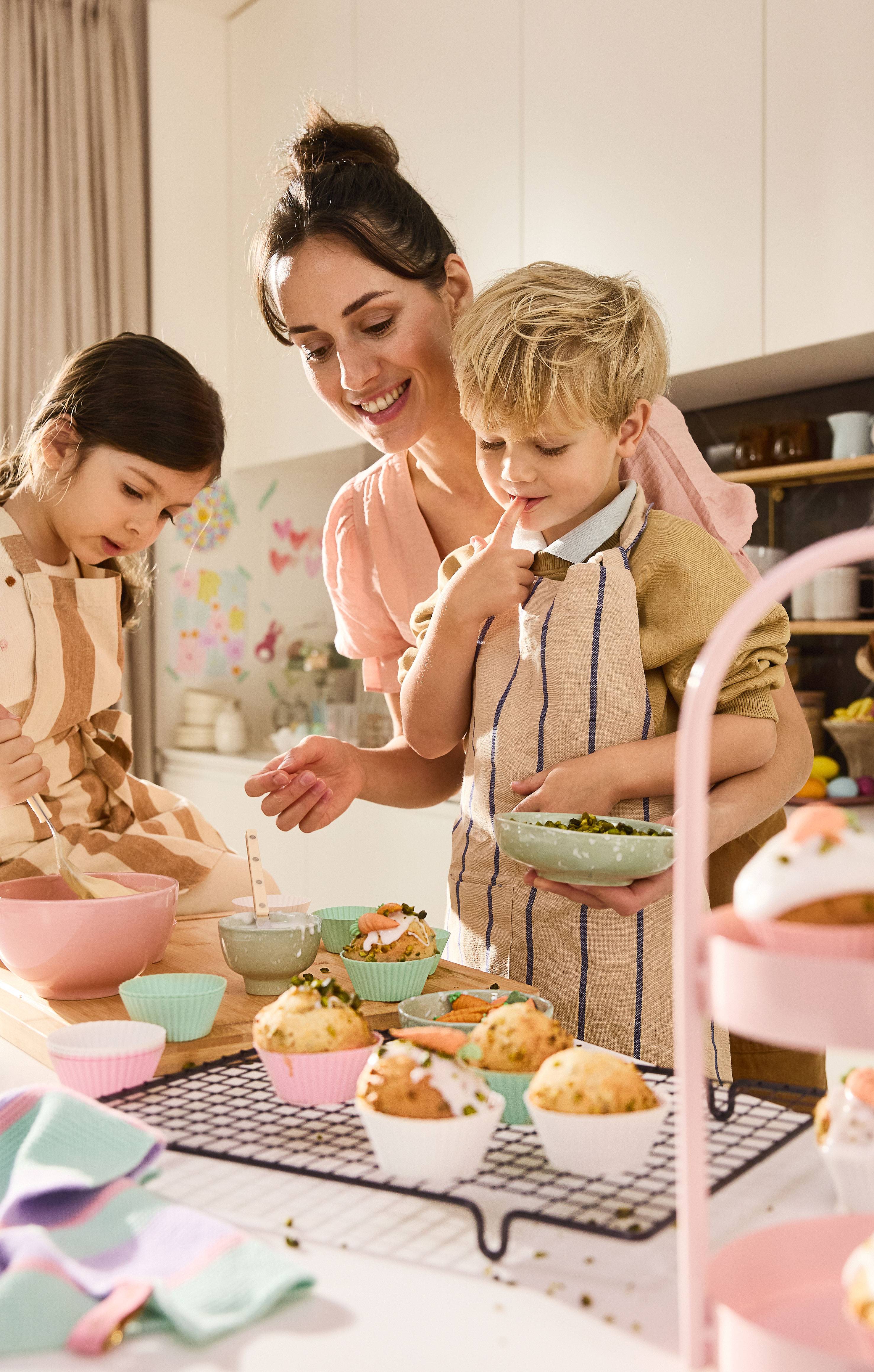 Moeder en kinderen versieren paasmuffins met glazuur en pistachenoten.