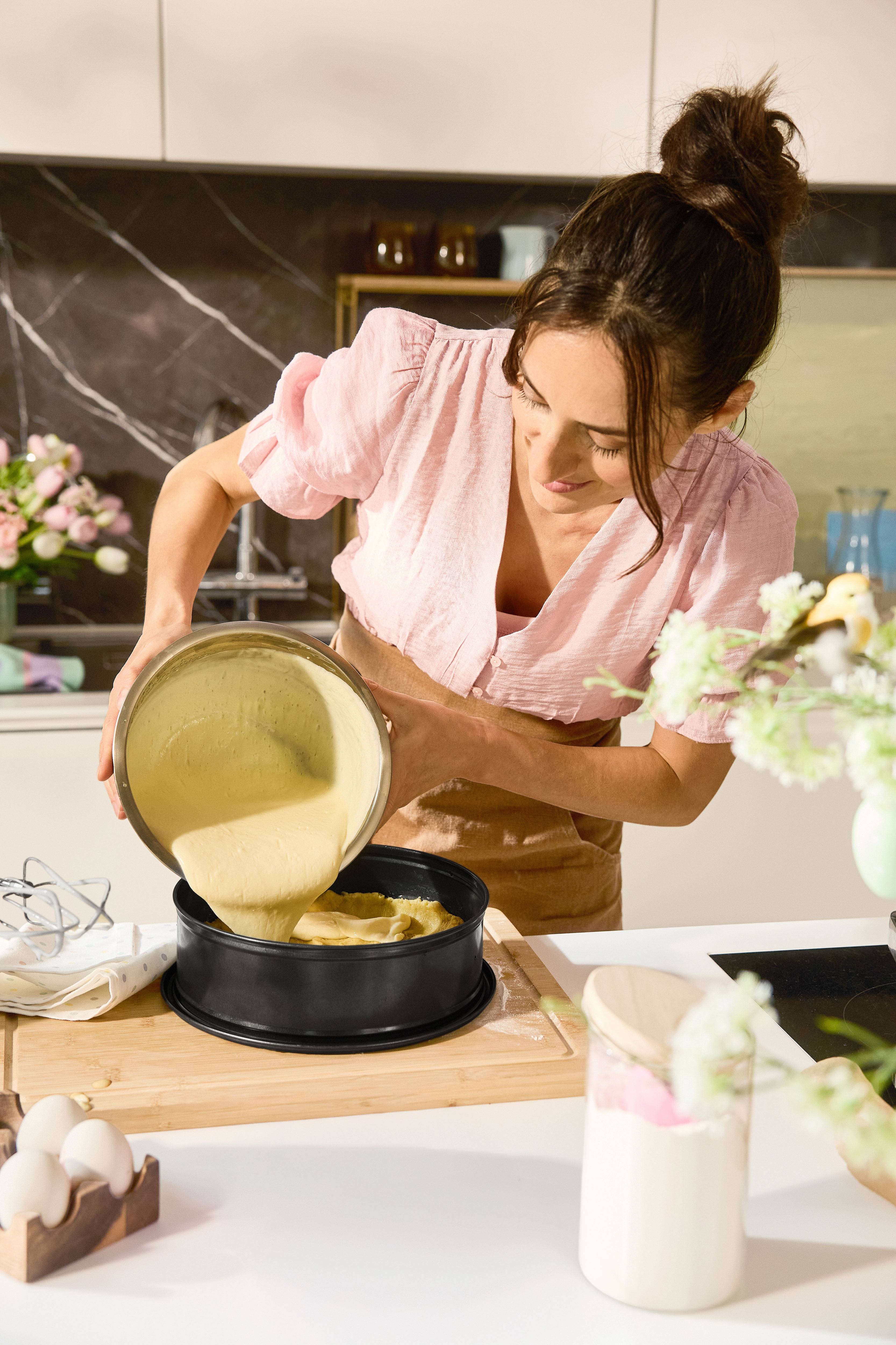 Vrouw giet beslag in bakvorm in de keuken.