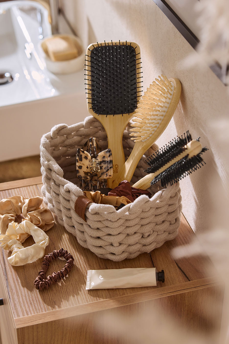 Haarborstels en haaraccessoires in een gevlochten mand op een houten oppervlak naast een wastafel.