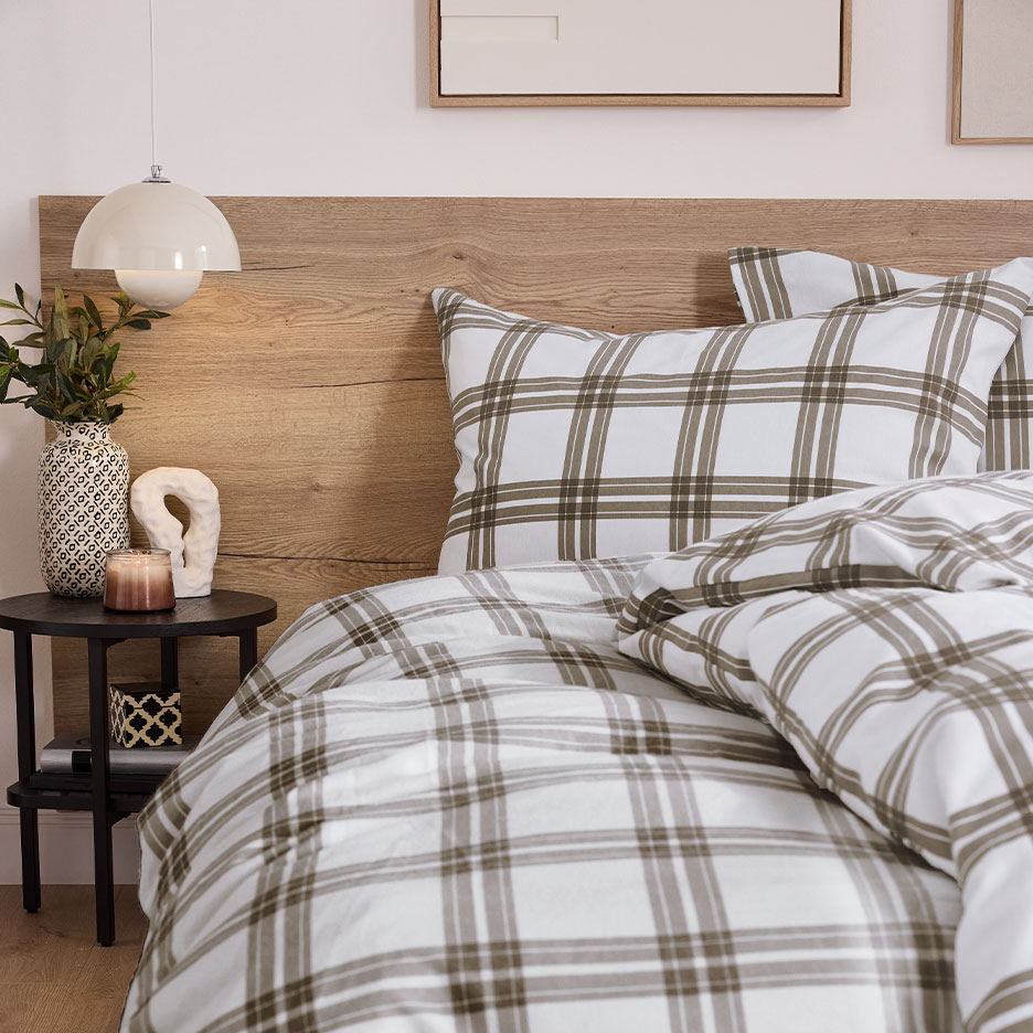 Bed met houten hoofdbord en geruit beddengoed, nachtkastje met lamp.