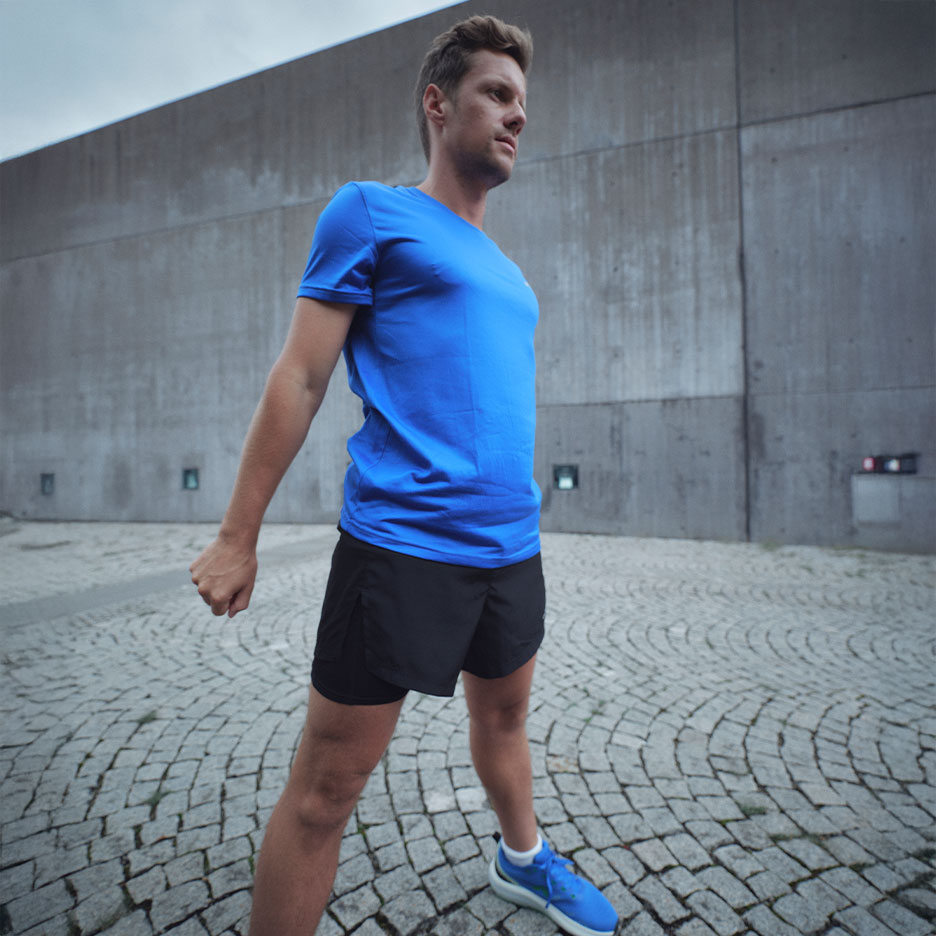 Homme en t-shirt bleu et short noir, se préparant à l'exercice.