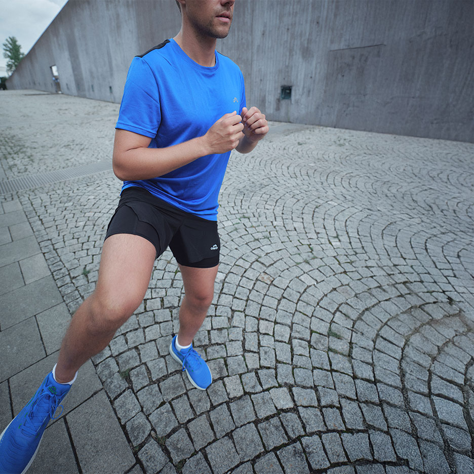Homme en t-shirt bleu et short de sport noir courant sur des pavés.