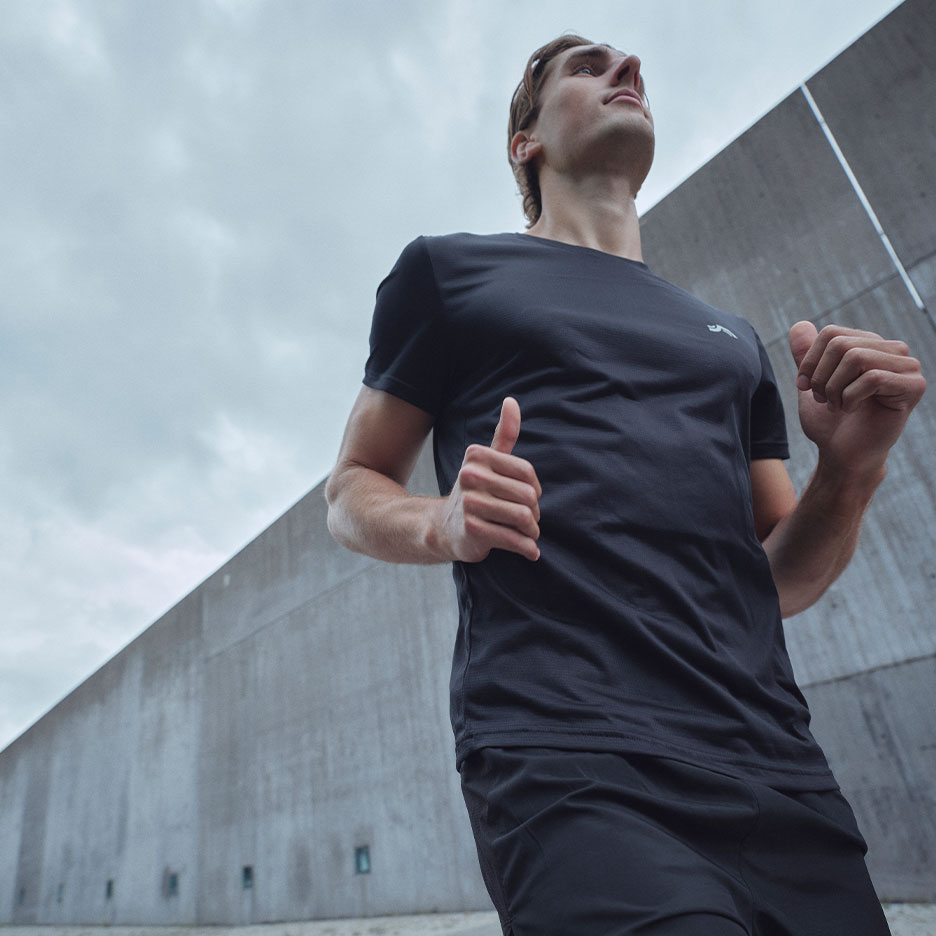 Homme en t-shirt et short de sport noirs courant en extérieur.