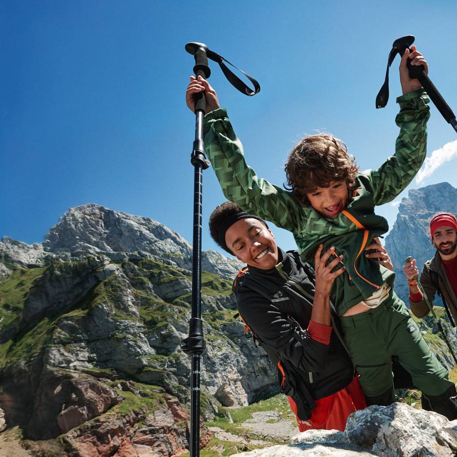 Familie wandelt met trekkingstokken en outdoorkleding in de bergen.
