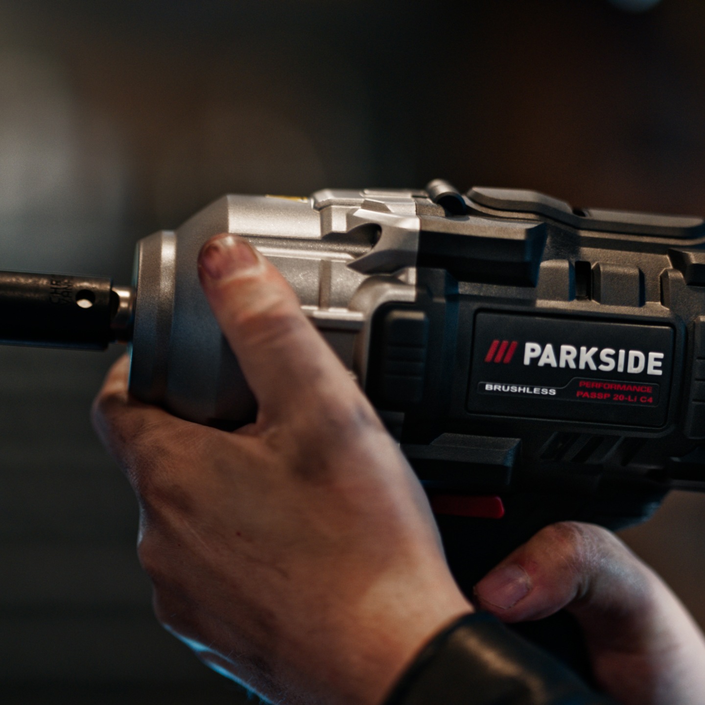 Een persoon houdt een Parkside Performance slagschroevendraaier vast, met vuile handen.