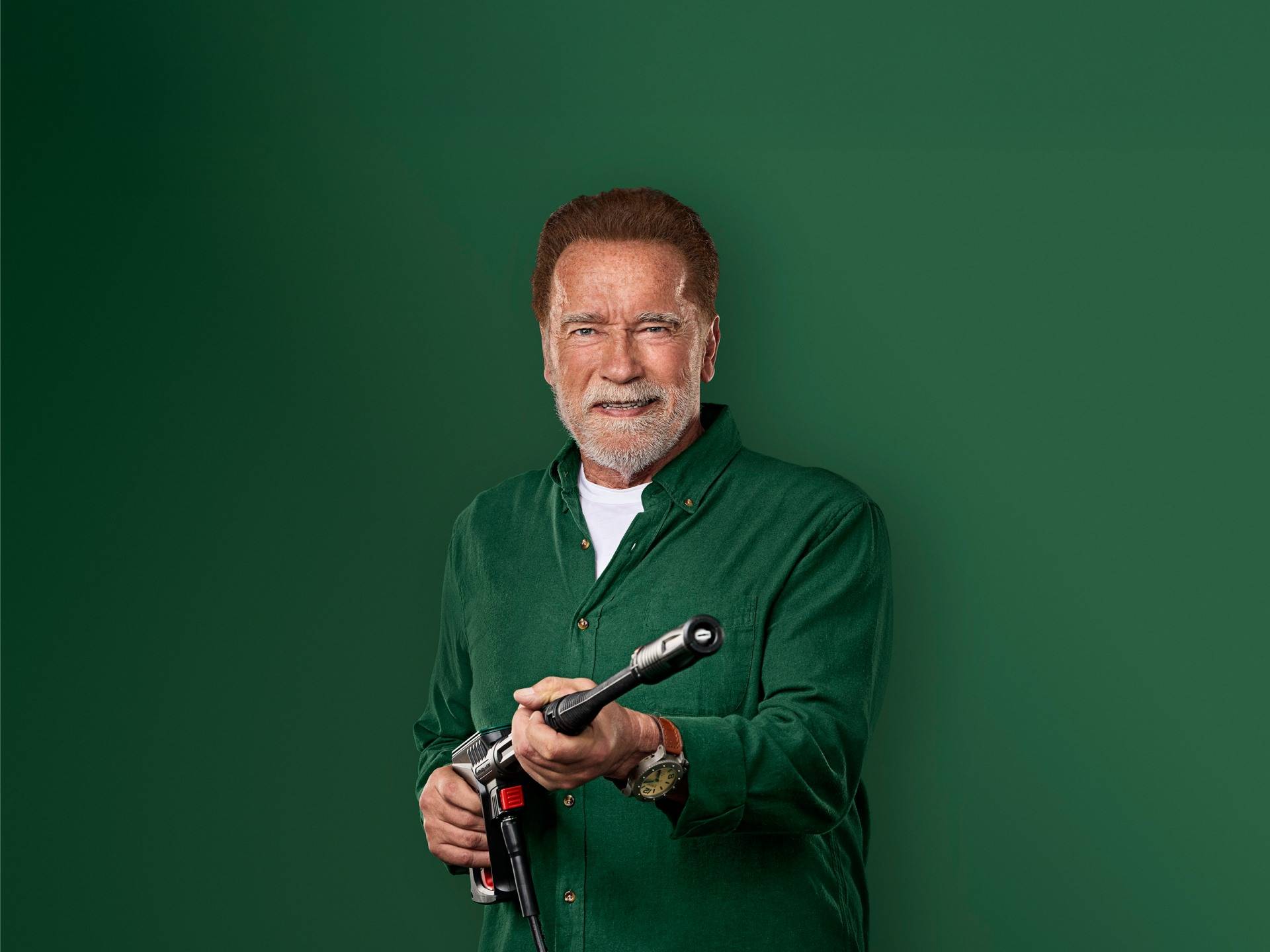 Arnold Schwarzenegger lacht, met een hogedrukreiniger in zijn hand.