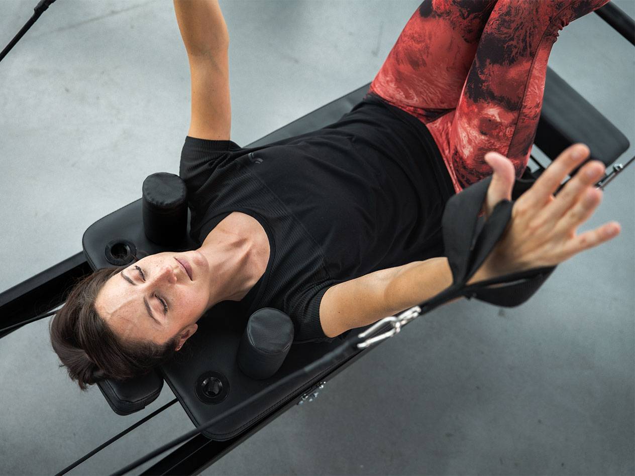 Vrouw in sportkleding ligt op een Pilates-apparaat en traint.