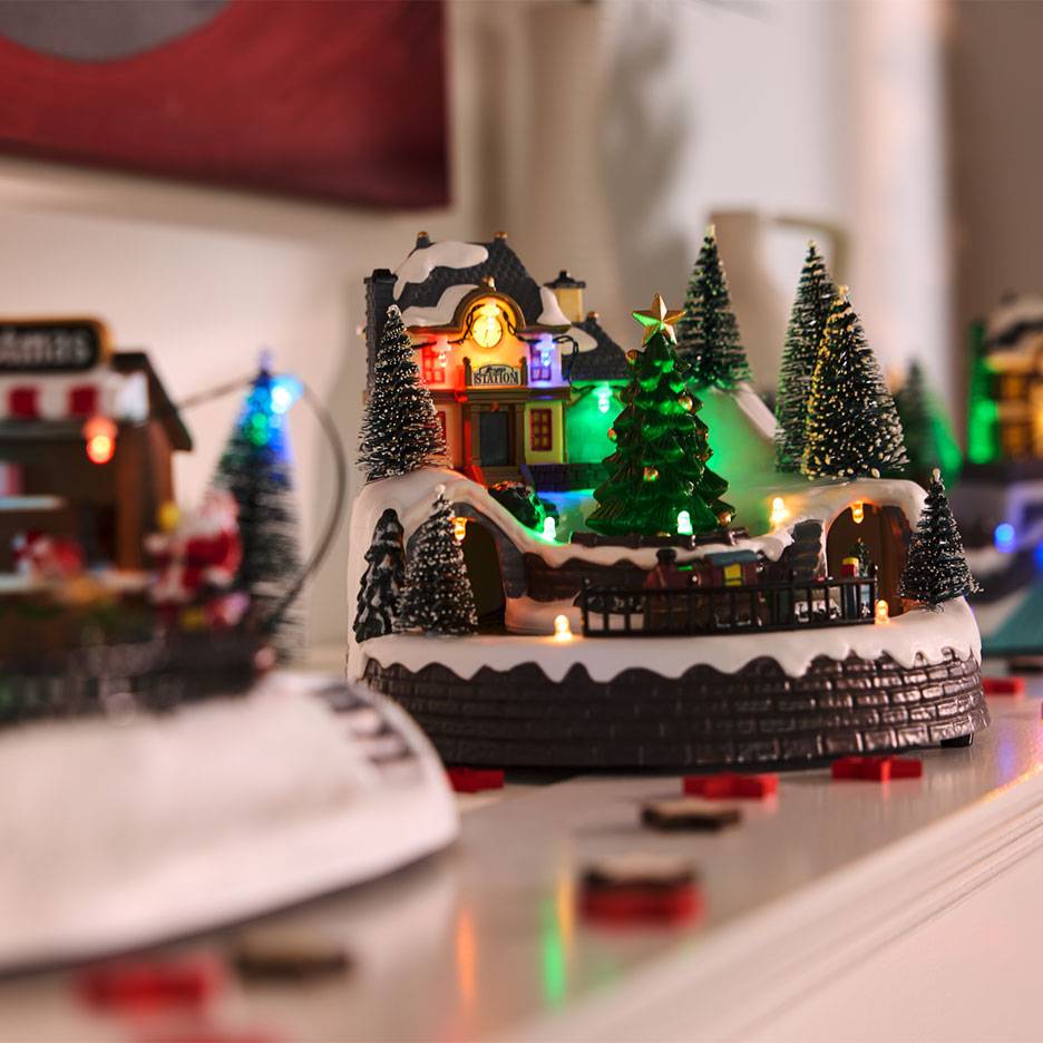 Kerstdorp met verlicht station, bomen en miniatuurspoorlijn.