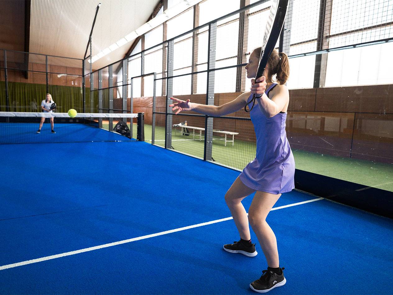 Lana Büttner in een paarse jurk speelt padel op een blauw terrein.