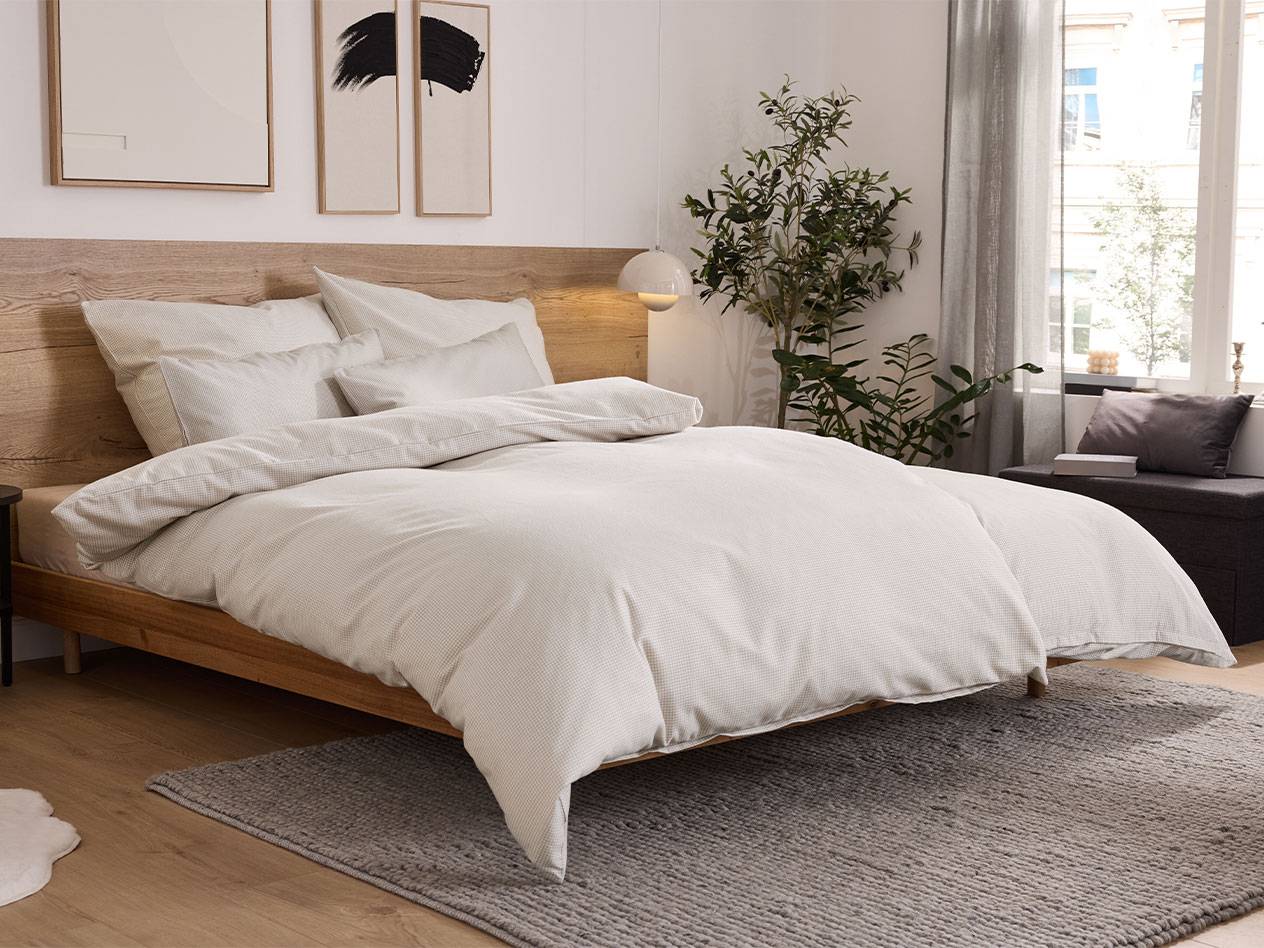 Slaapkamer met houten bed, wit beddengoed en grijs vloerkleed.
