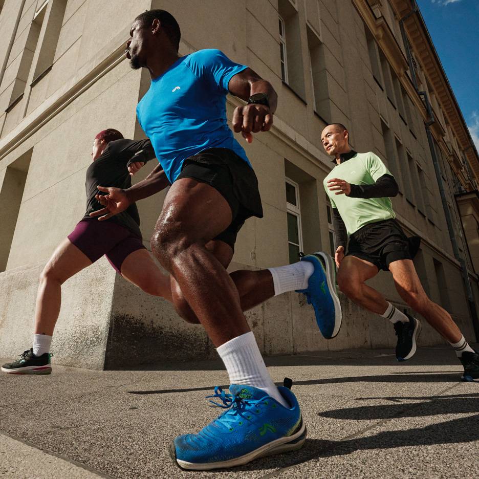 Drie hardlopers in sportshirts en shorts rennen door een stadsstraat.