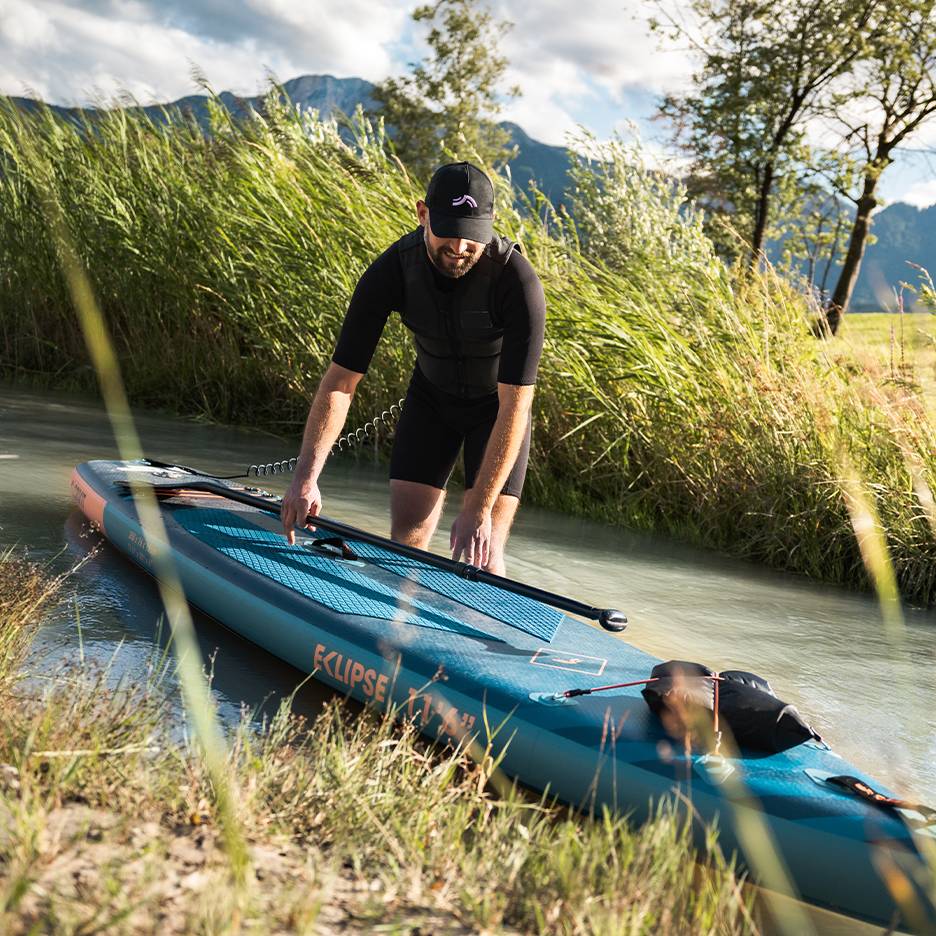Man in zwart wetsuit bereidt zich voor op paddleboarden, board in het water