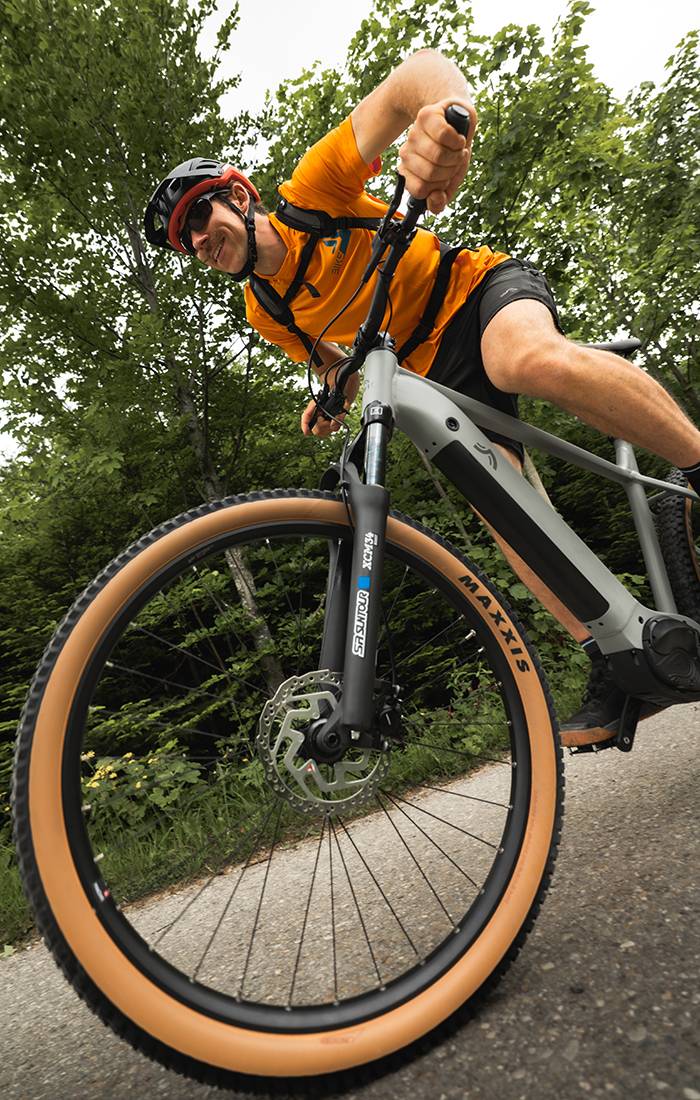 Een man fietst op een grijze Maxxis e-bike door een bos.