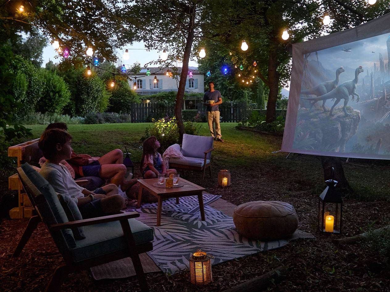 Familie geniet van een buitenfilmavond met lichtslingers en comfortabel tuinmeubilair.