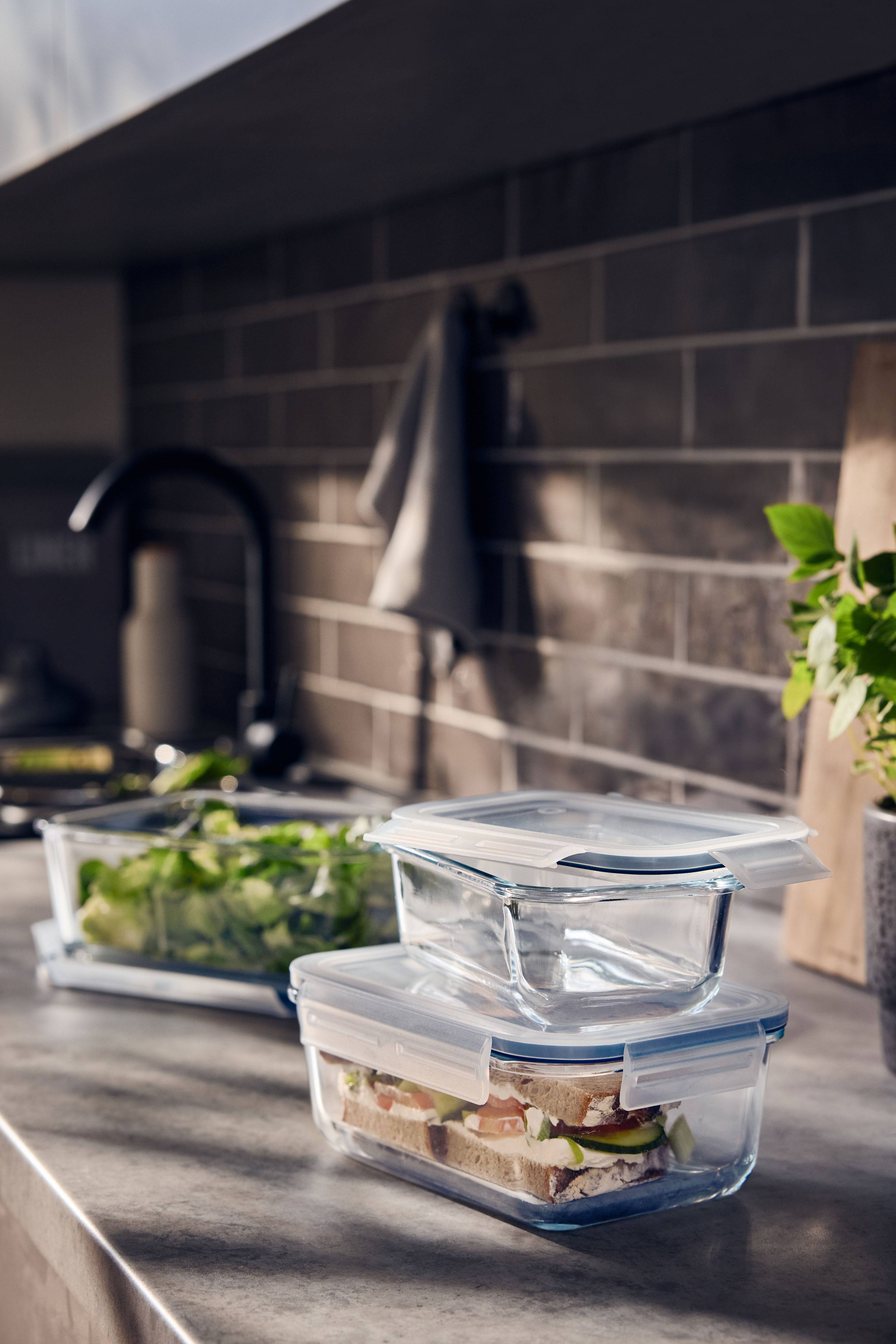 Glazen containers met deksels, één met een sandwich en één met salade, in een keuken.