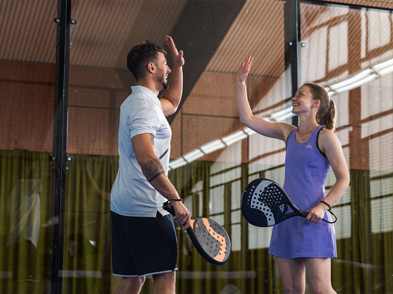 Twee padelspelers in sportkleding geven elkaar een high-five op de baan.