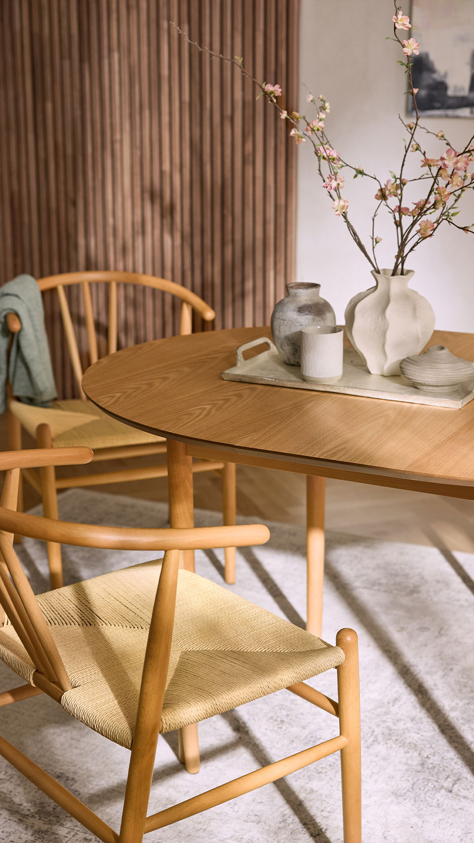 Houten eettafel met stoelen, vazen en bloeiende takken op een dienblad.