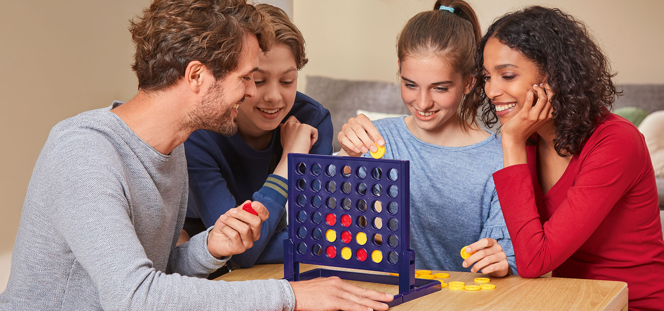 Quatre personnes jouant au jeu de société Connect 4 à une table en bois.