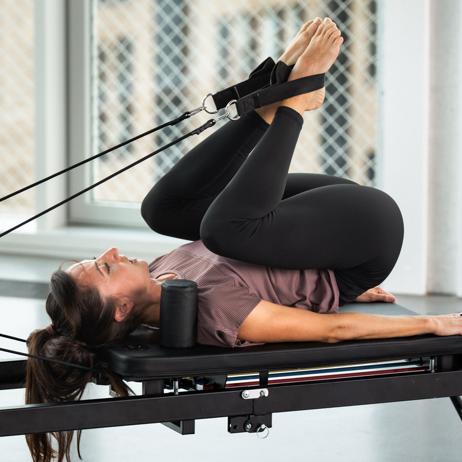Vrouw doet Pilates op een reformer met haar benen in de banden.