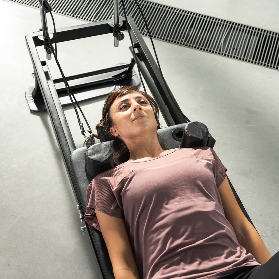 Vrouw ligt op een fitnessapparaat, omhoog kijkend.