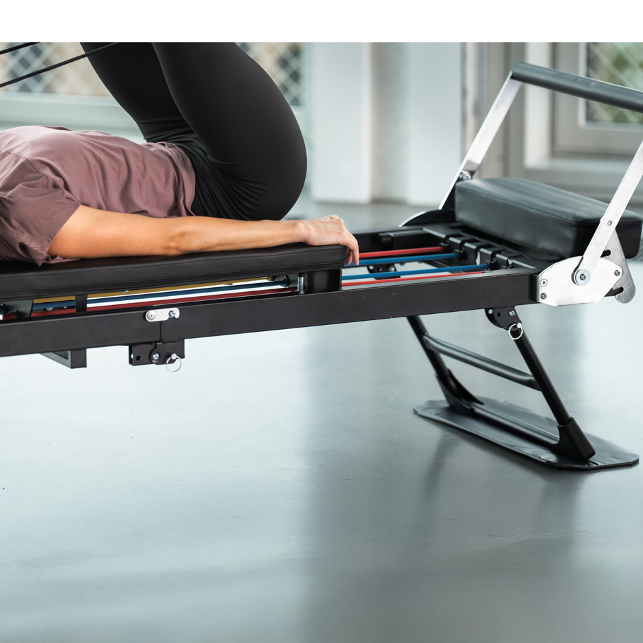 Vrouw traint op een zwarte Pilates-machine met gekleurde weerstandsbanden.