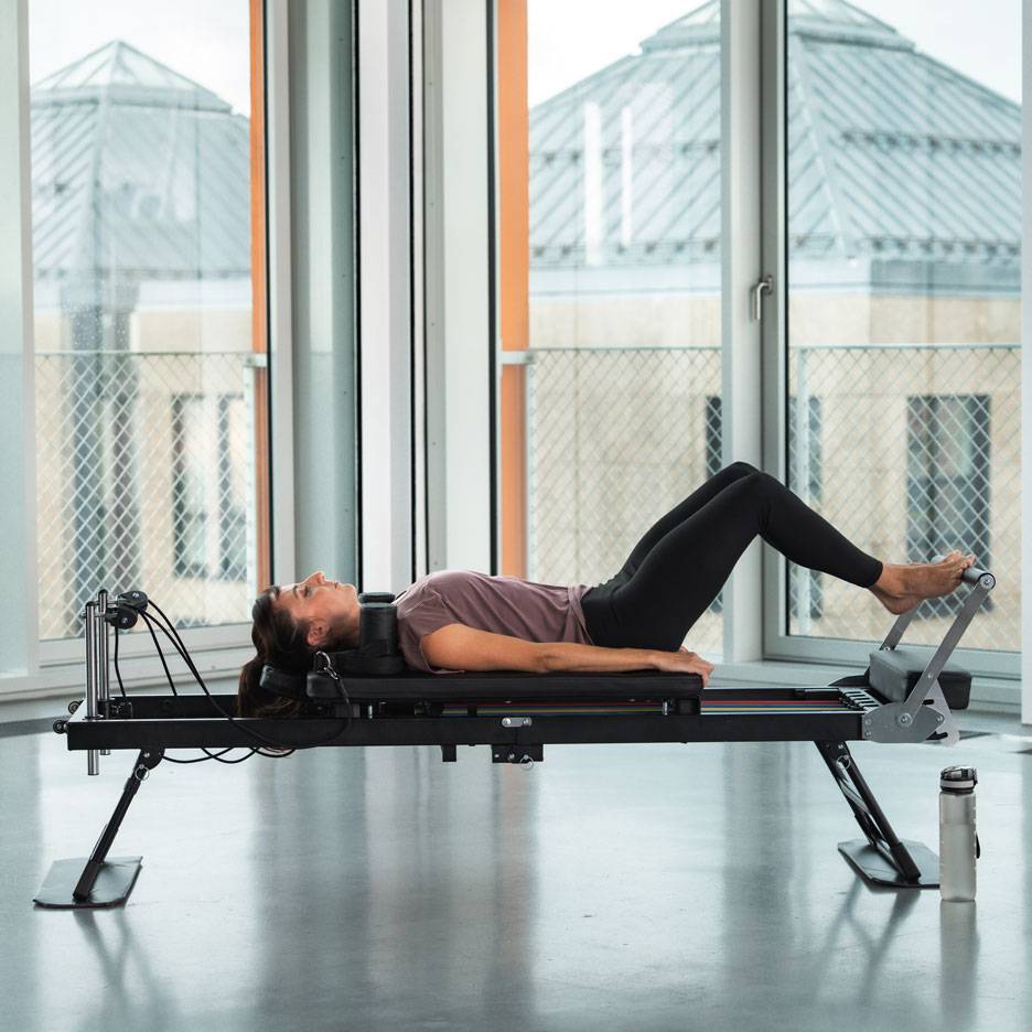 Vrouw doet Pilates-oefeningen op een reformer-apparaat.