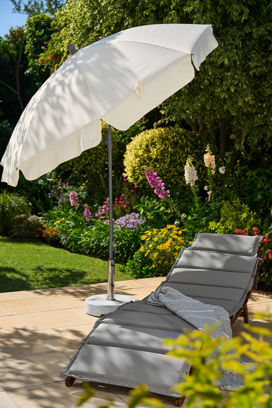 Tuinparasol en ligstoel met kussen en plaid op een terras.