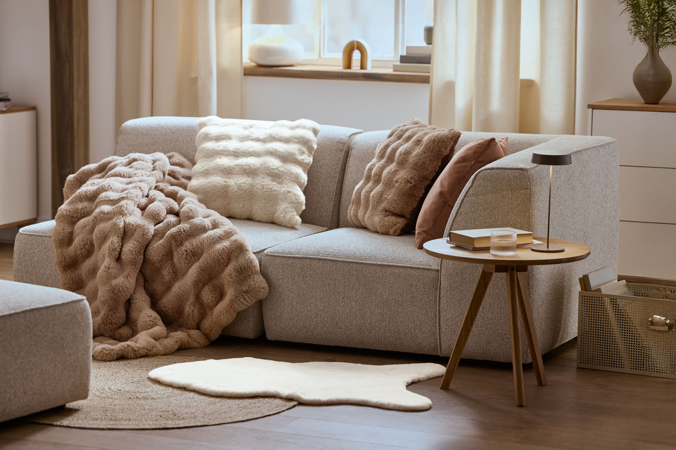 Salon confortable avec un canapé gris, des coussins et une couverture moelleux, une table basse en bois.