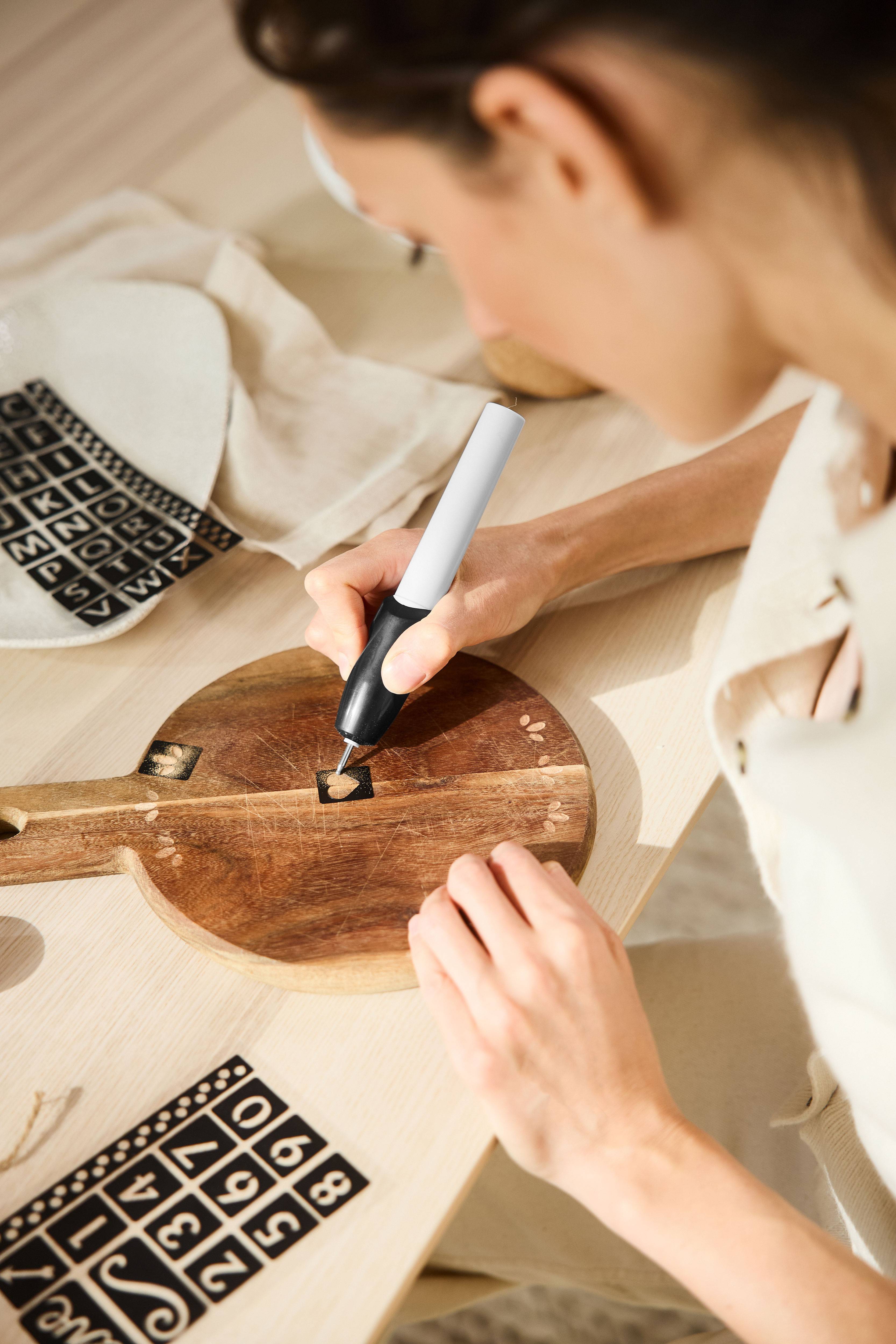 Vrouw graveert houten plank met graveerpen en sjablonen.