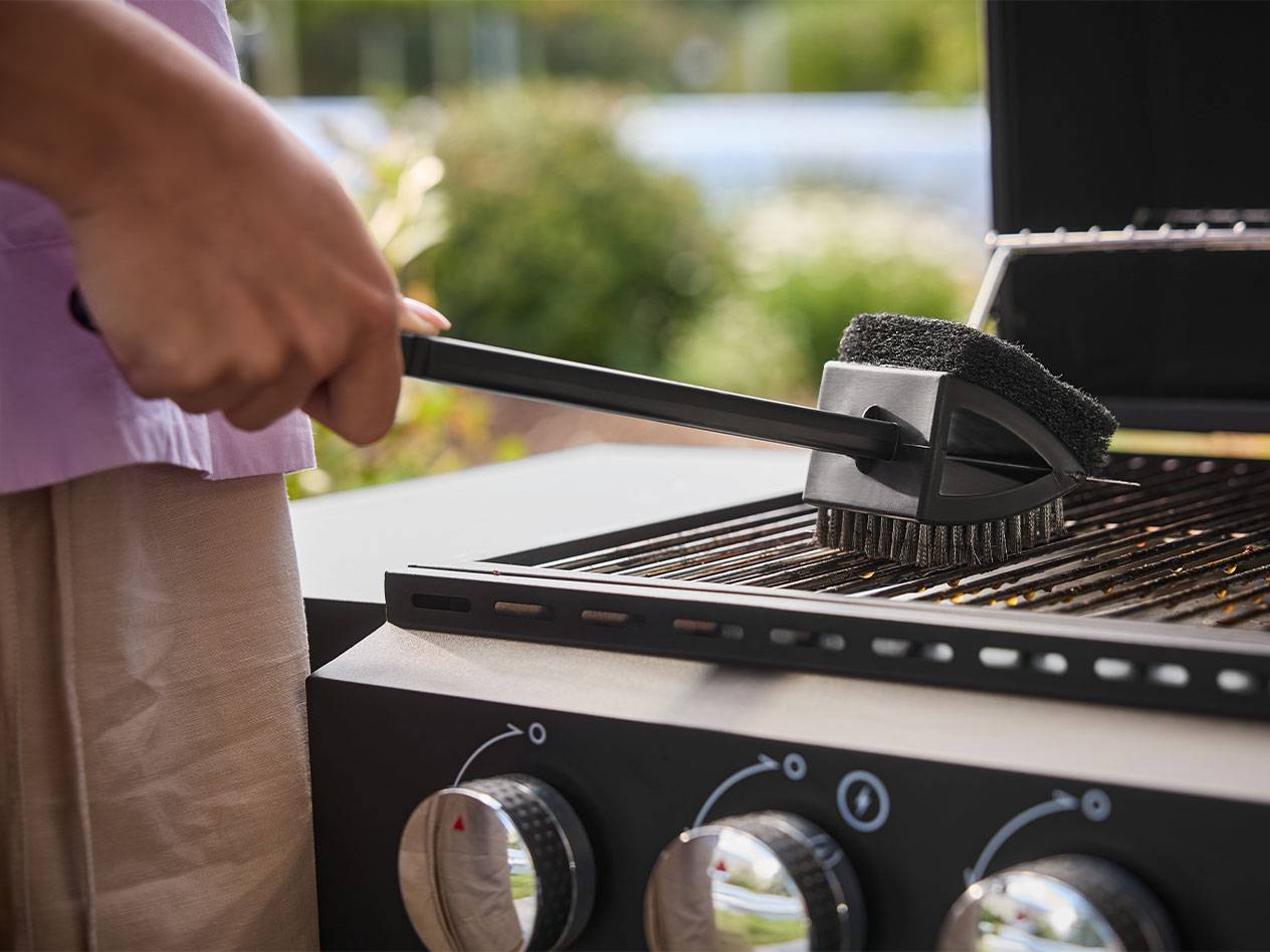 Persoon die een barbecuegrill schoonmaakt met een borstel met lange steel.