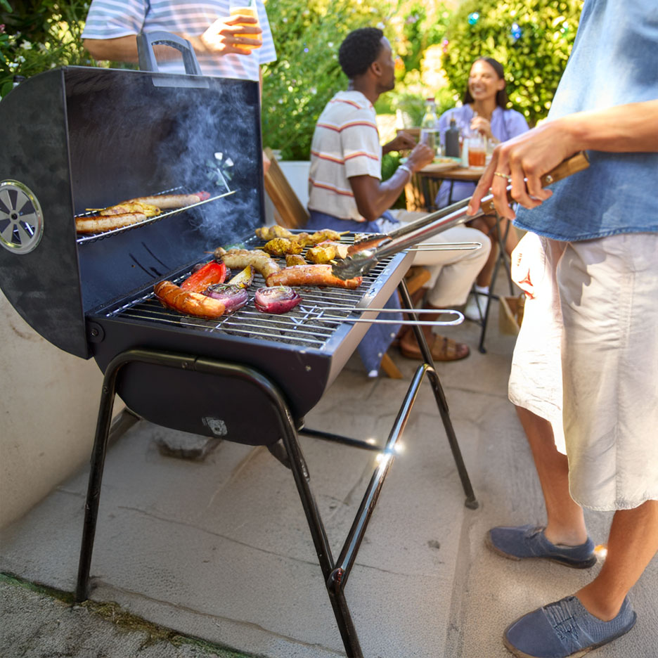 Een buitenbarbecue met gegrilde worsten, groenten en vlees.