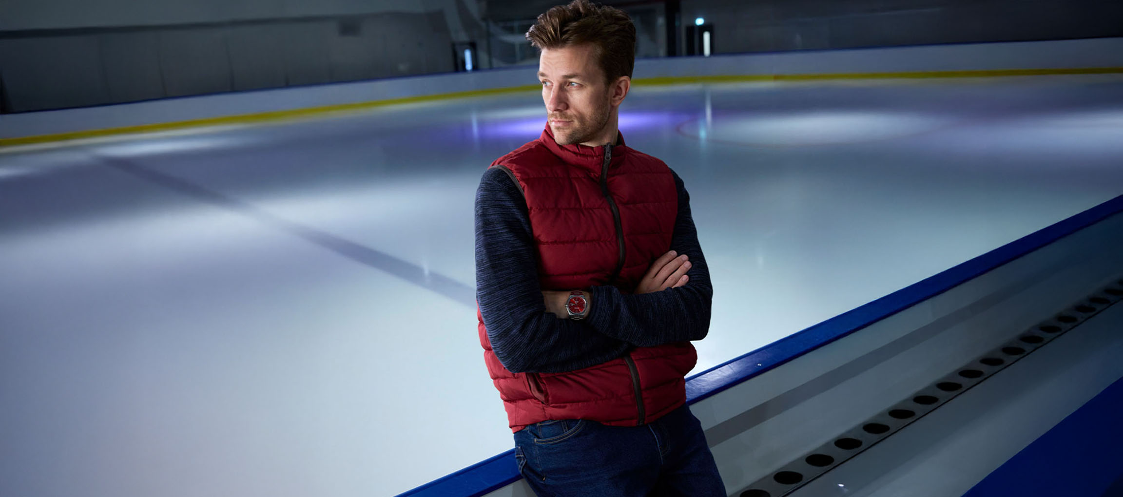 Homme en gilet rouge et pull bleu sur une patinoire