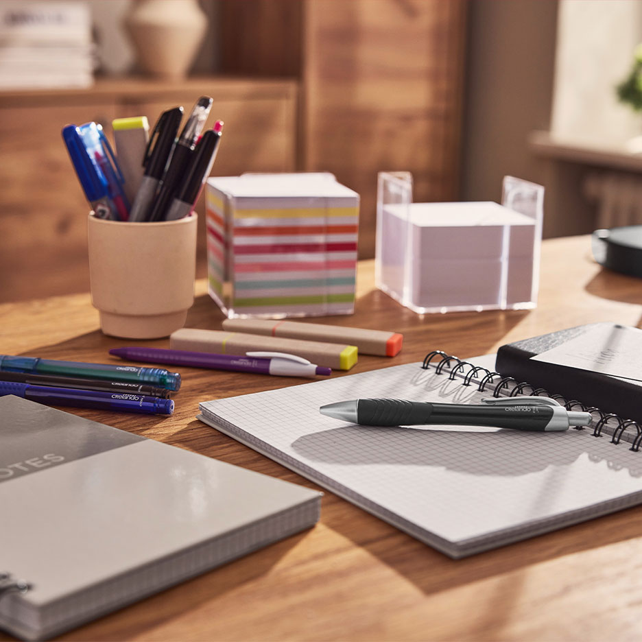 Bureau met notitieboekjes, pennen, markeerstiften en plaknotities.
