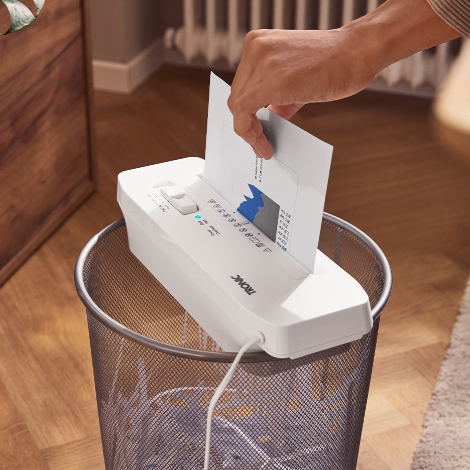 Hand voert papier in een TRONIC papierversnipperaar bovenop een prullenbak.