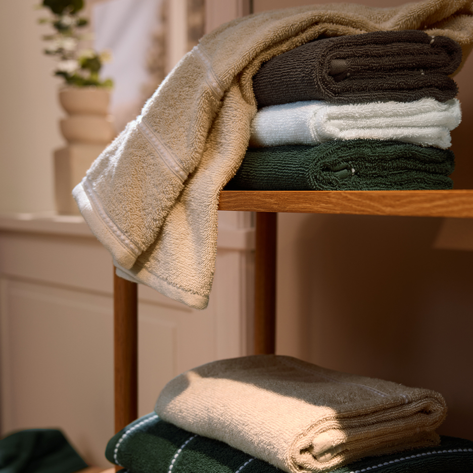 Gestapelde beige, donkerbruine, witte en donkergroene handdoeken op een houten plank.