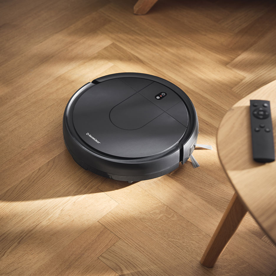 Aspirateur robot sur un parquet en bois à côté d'une télécommande.