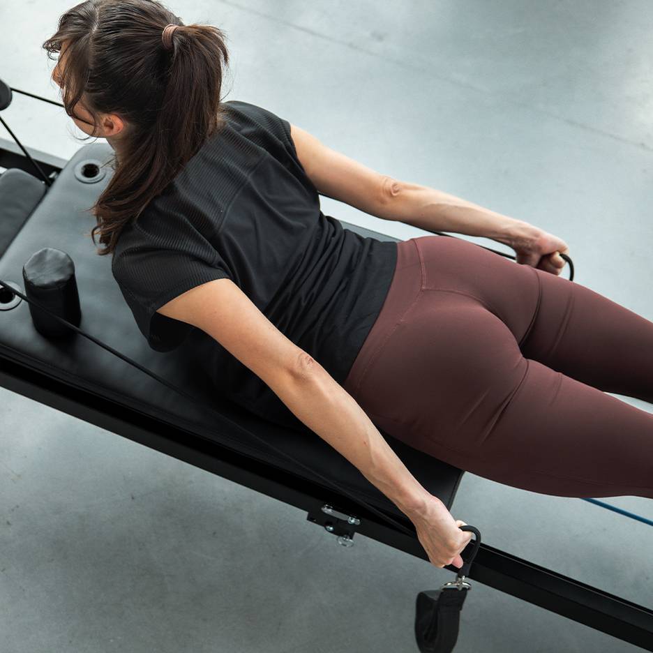 Vrouw traint op een Pilates-apparaat met weerstandsbanden, gekleed in sportkleding.