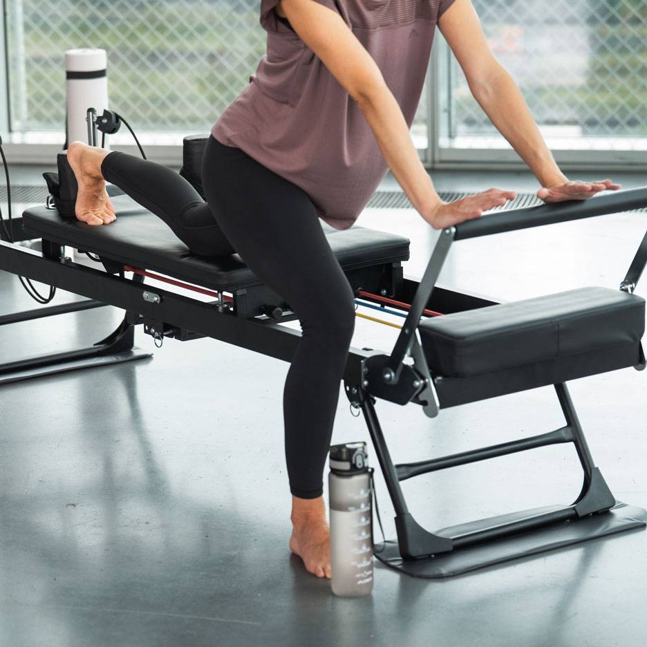 Vrouw sport op een Pilates-apparaat met een waterfles ernaast.
