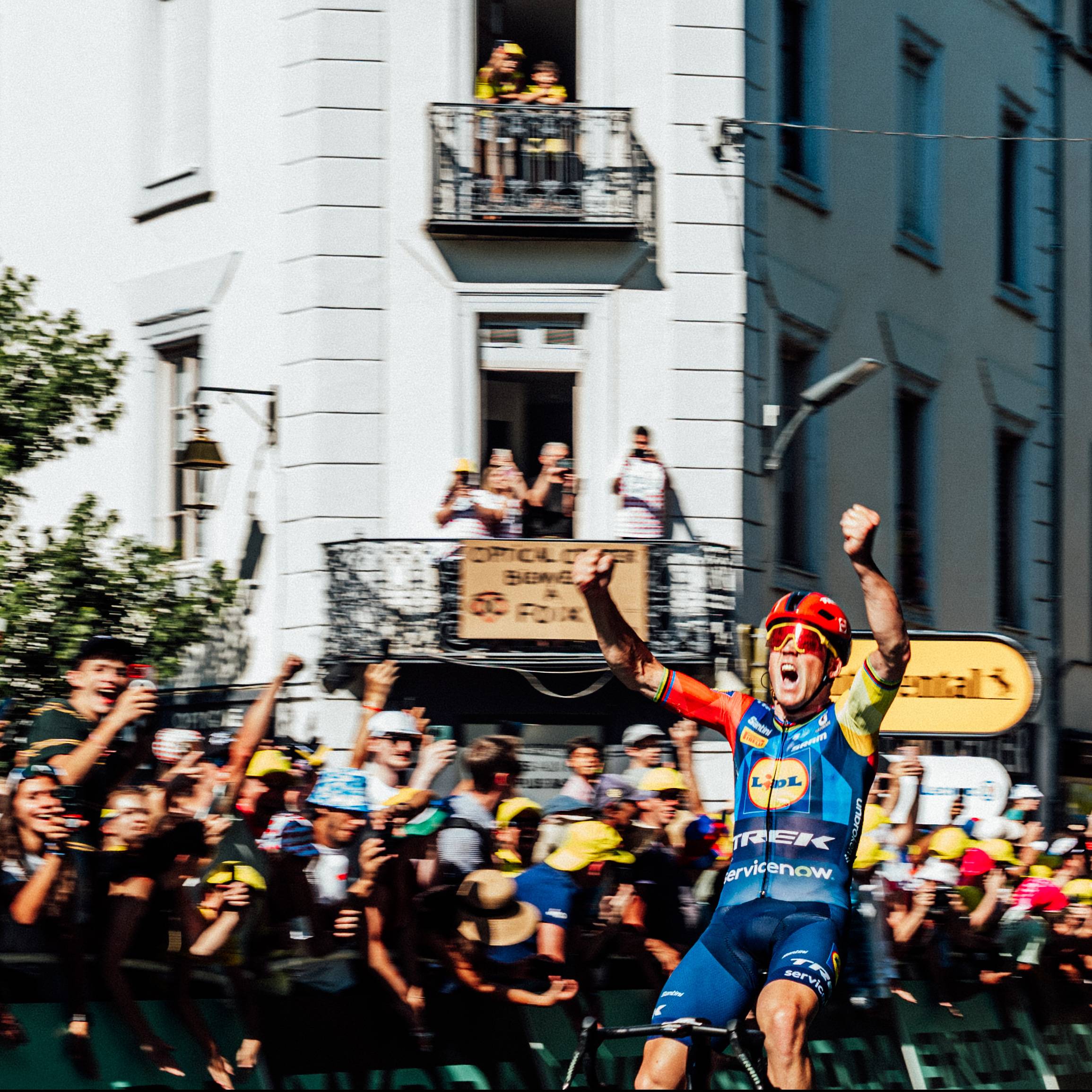 Cycliste célèbre sa victoire devant la foule, avec des balcons en arrière-plan.