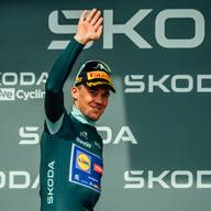 Cycliste en maillot vert et casquette, saluant la foule sur un podium.