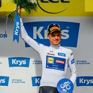 Cycliste joyeux en maillot blanc avec bouquet de fleurs et ruban bleu sur le podium.