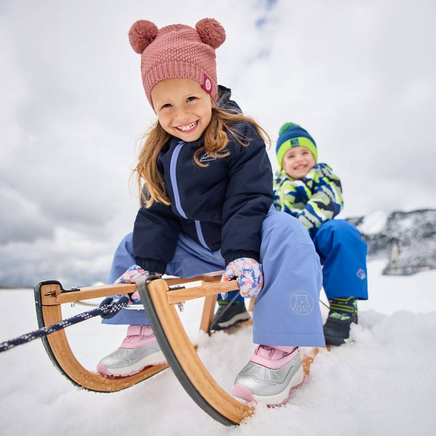 Kinderen in winterkleding en mutsen met pompons, sleeën in de sneeuw.