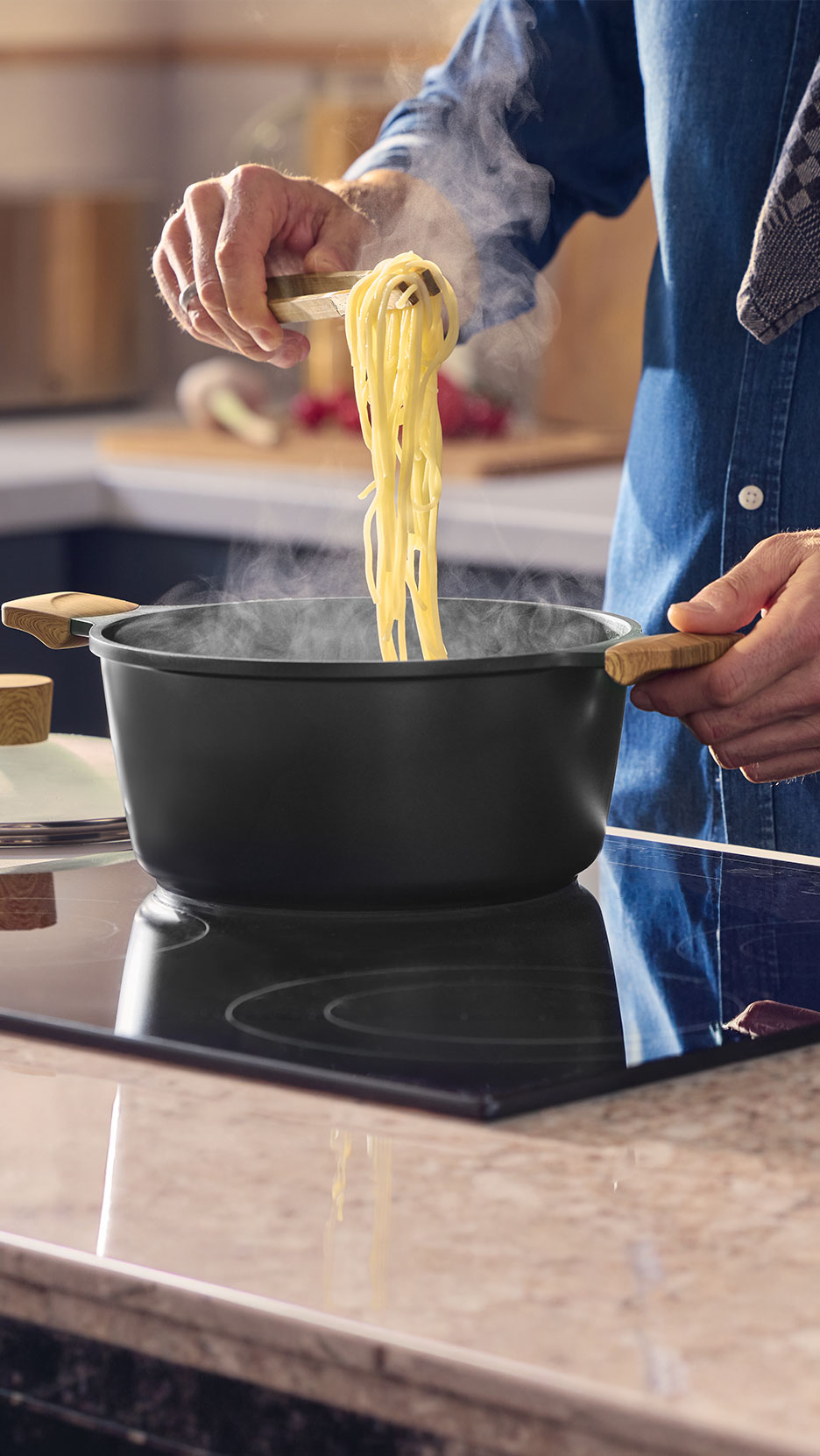 Chef soulevant des spaghettis avec des pinces d'une casserole noire sur une plaque.