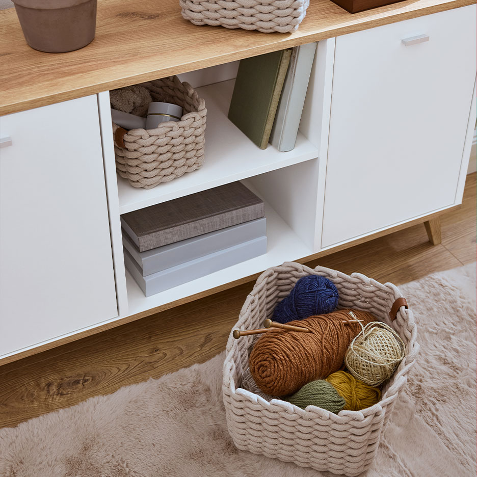 Houten opbergmeubel met gevlochten manden en breigarens.