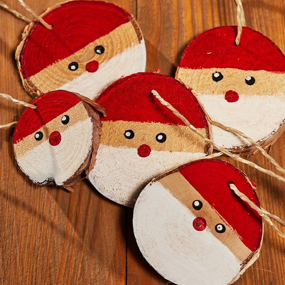Vijf handgeschilderde kerstmanornamenten van houten schijfjes met touwtjes, liggend op een houten tafel.
