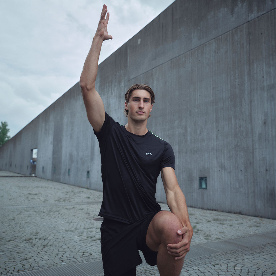 Man in zwart sport T-shirt en korte broek rekt zich buiten uit.