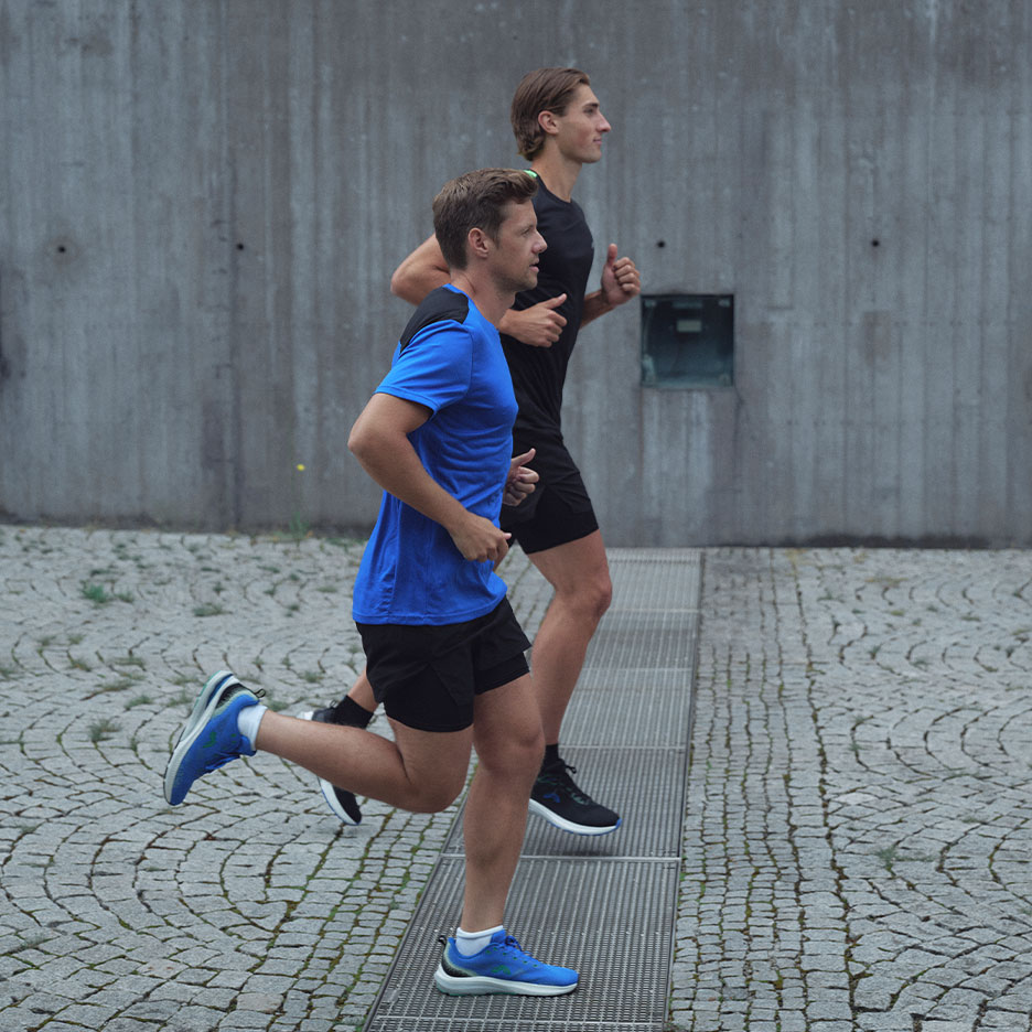 Twee mannen in sportkleding rennen buiten op een geplaveide straat.