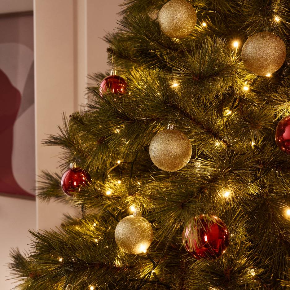 Kerstboom versierd met glimmende gouden en rode kerstballen en warme lichtslingers.